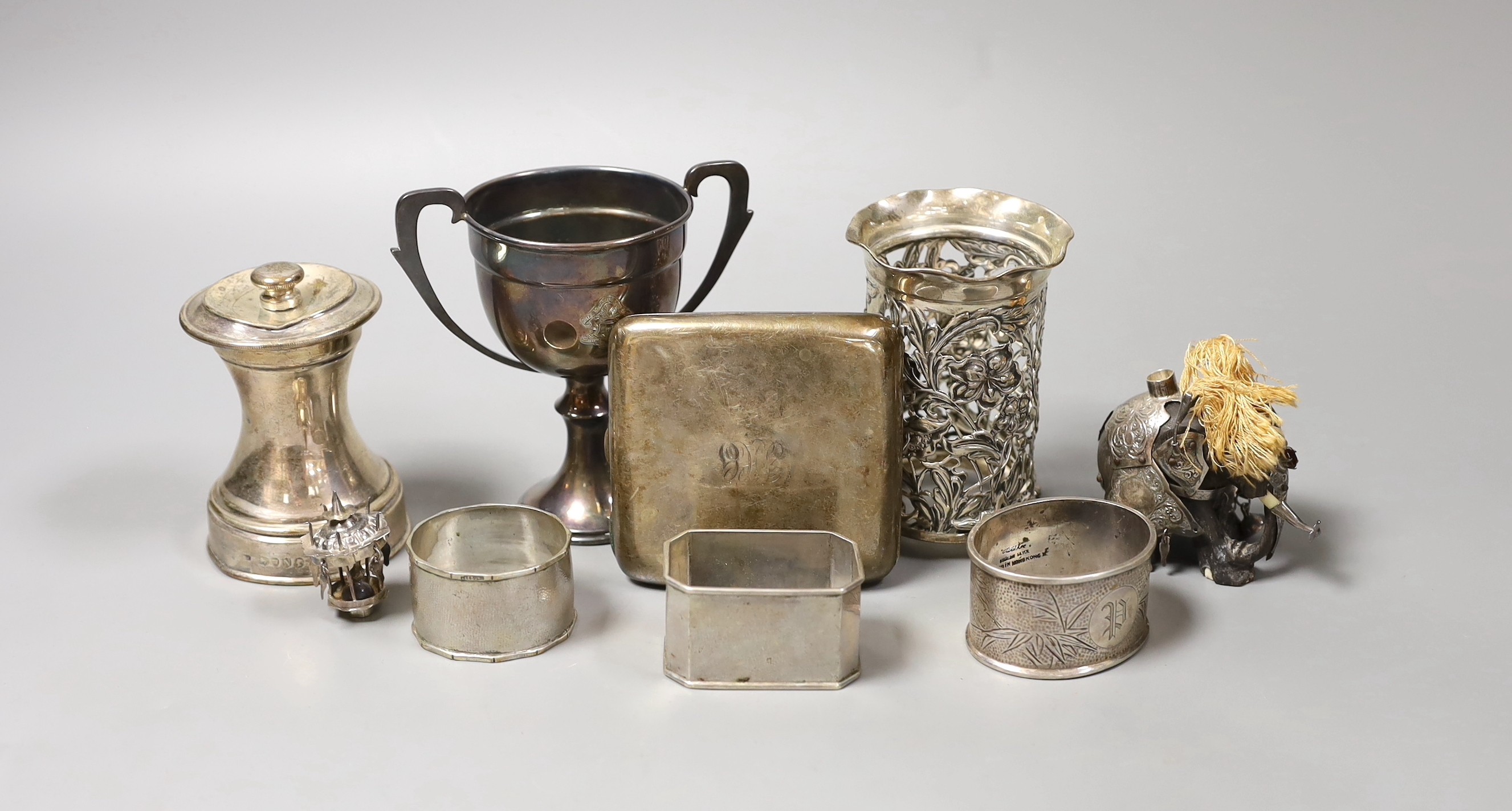 Sundry small silver including a late Victorian silver mounted pepper grinder, a paired silver vase, two handle trophy cup and a cigarette case, together with a white metal mounted miniature elephant with howdah and three